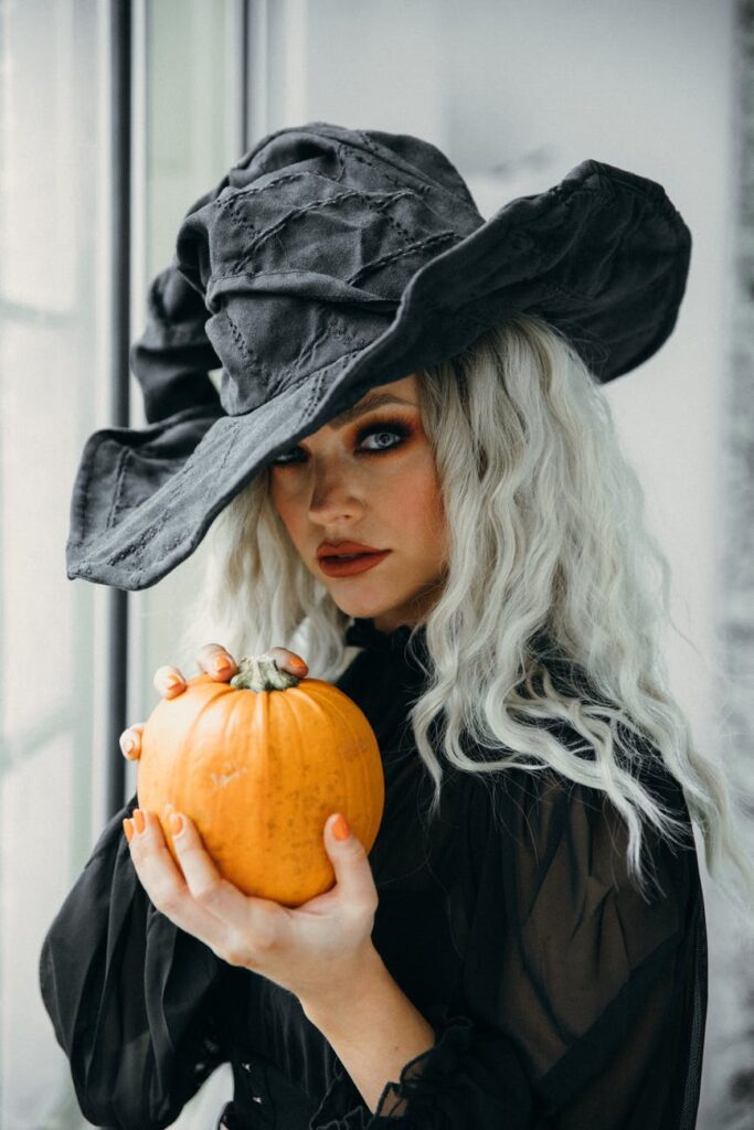 woman in black witch hat and dress while holding a halloween pumpkin