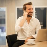 smiling formal male with laptop chatting via phone