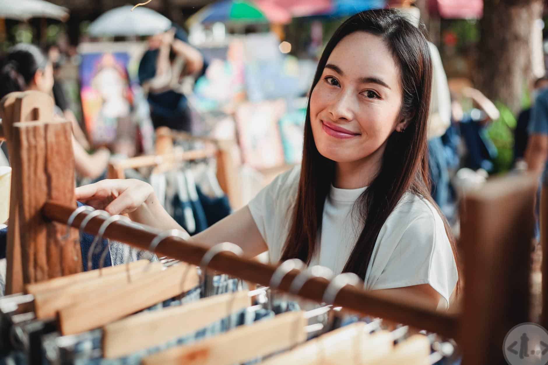 beautiful asian woman standing near rack with clothes in market