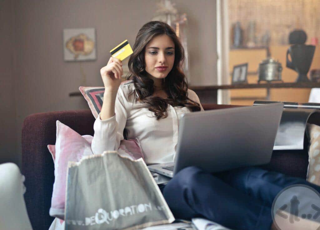 woman holding card while operating silver laptop