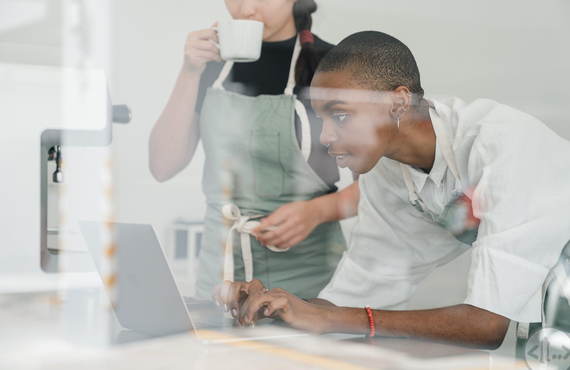 black female barista together with colleague using laptop at work