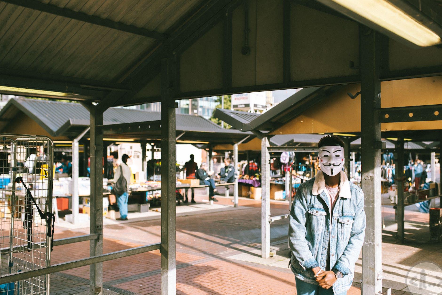confident african american man in anonymous mask standing in local market