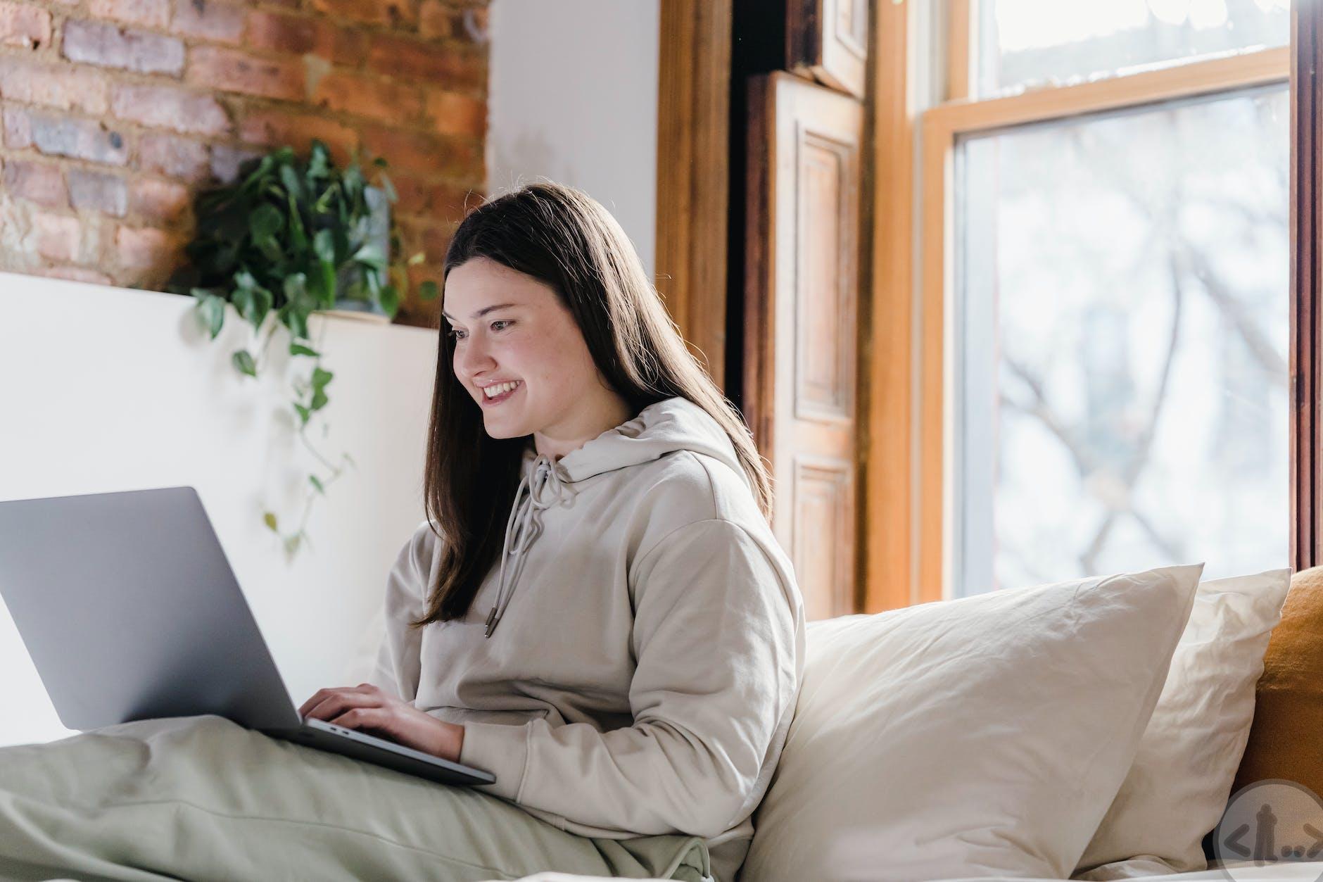 positive woman browsing laptop in bedroom during remote work