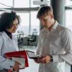 colleagues standing in white long sleeve shirts calculating financial report using a calculator